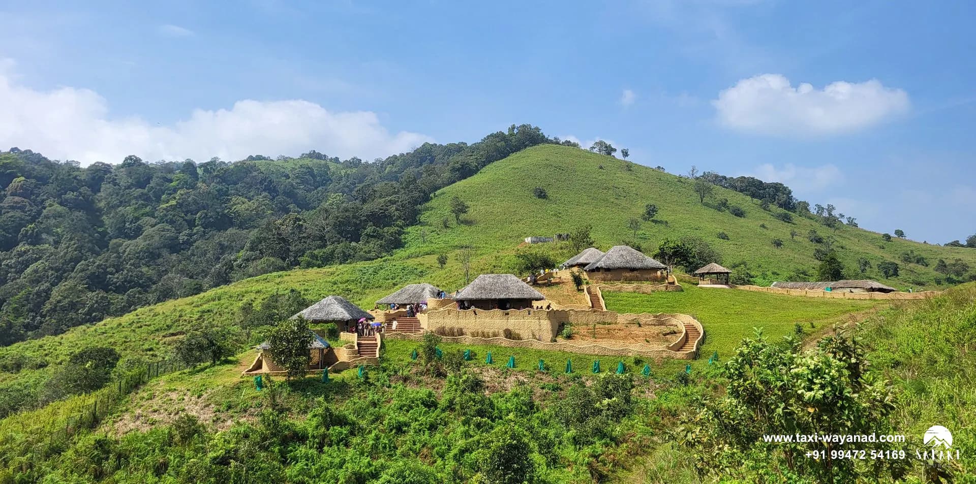 Thatched huts of the En Ooru tribal heritage village on a green hillside, Wayanad