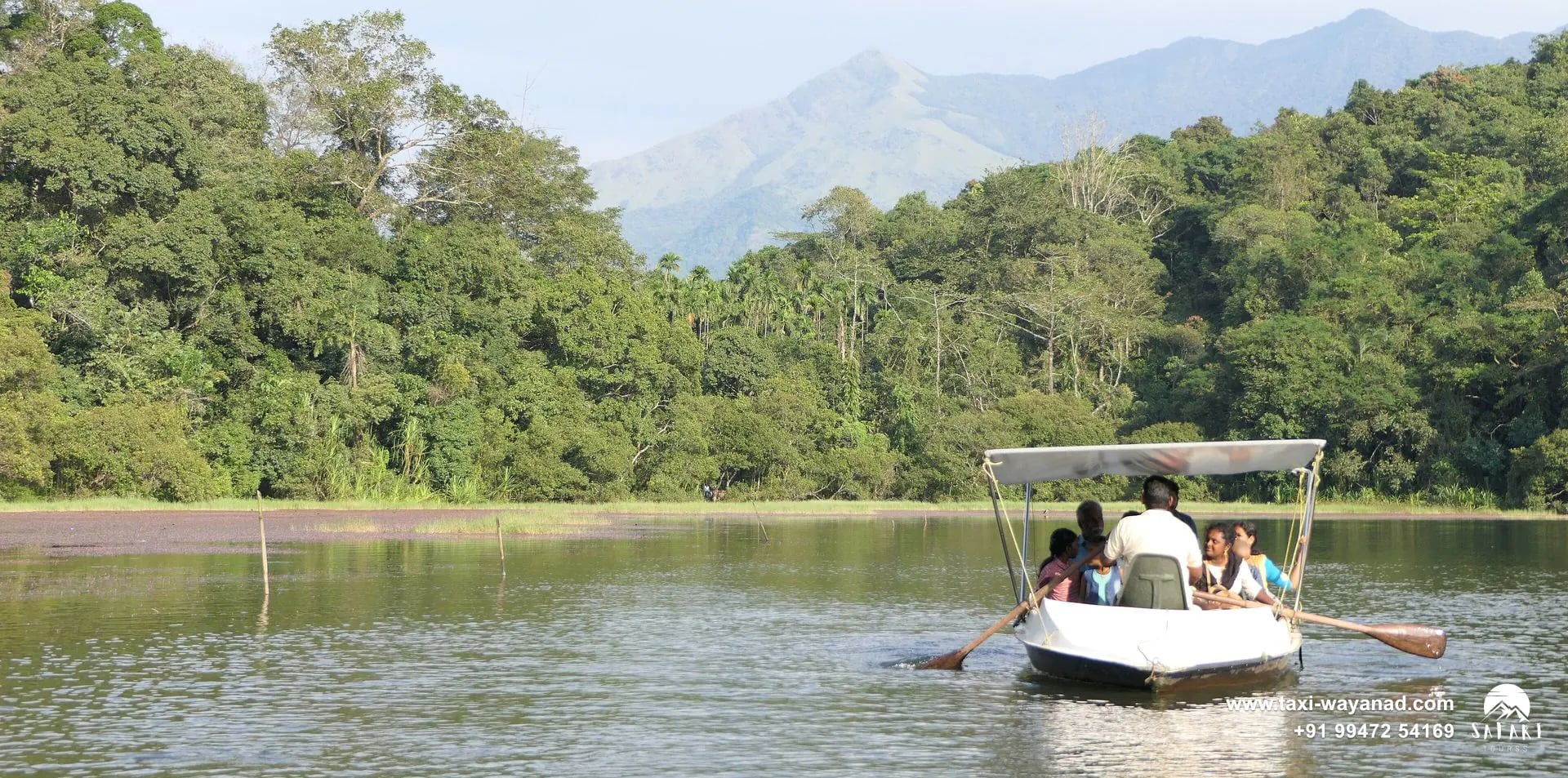 Visitors in a rowing boat below forest and a distant peak at Pookode Lake, Wayanad