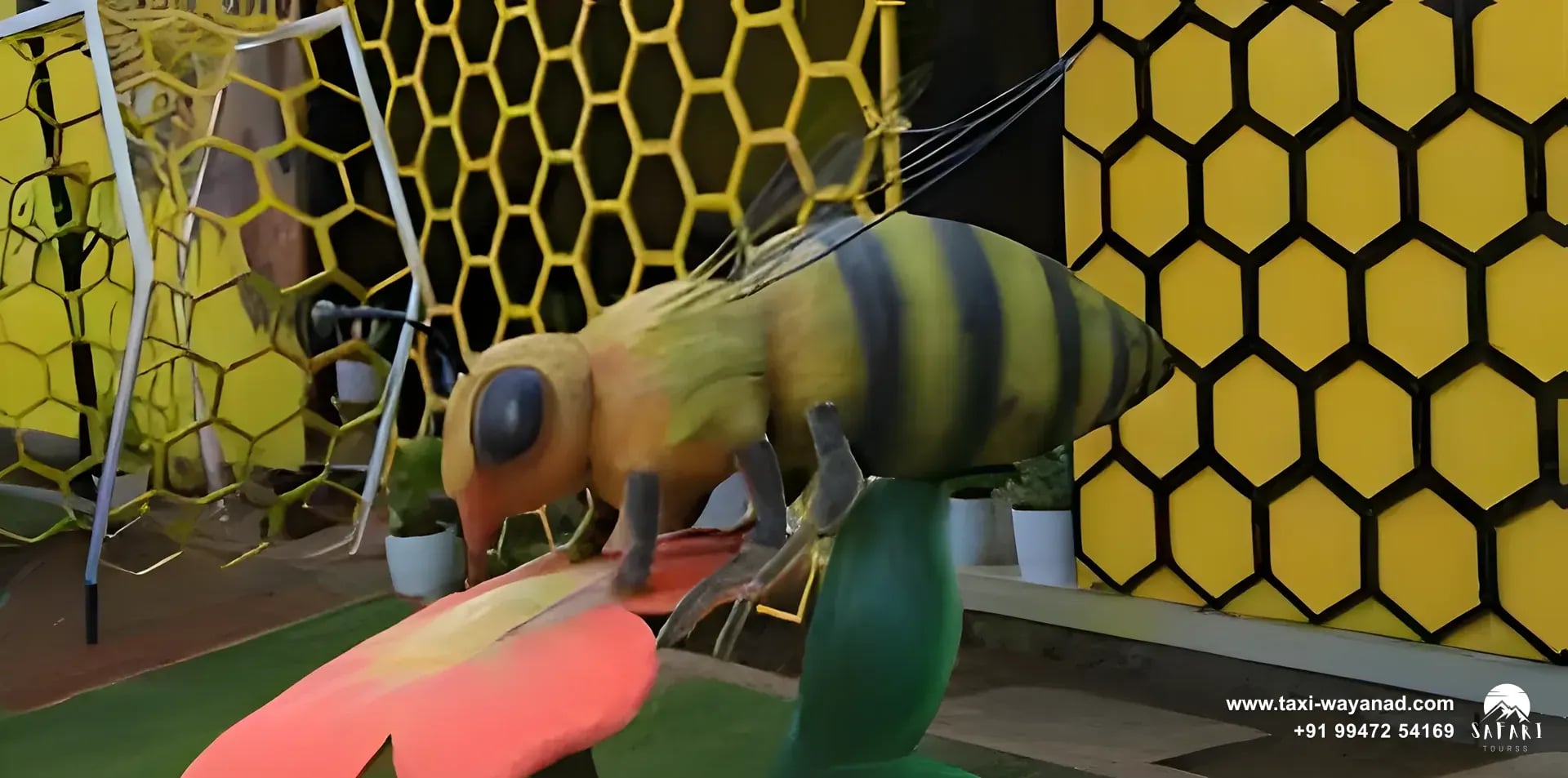 Large bee sculpture on a flower beside honeycomb walls at the honey museum, Wayanad