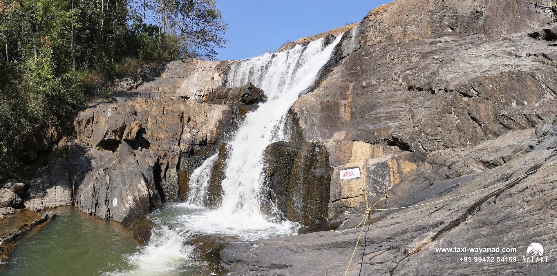 Kanthanpara Waterfalls pouring between broad granite slabs under a blue sky, Wayanad