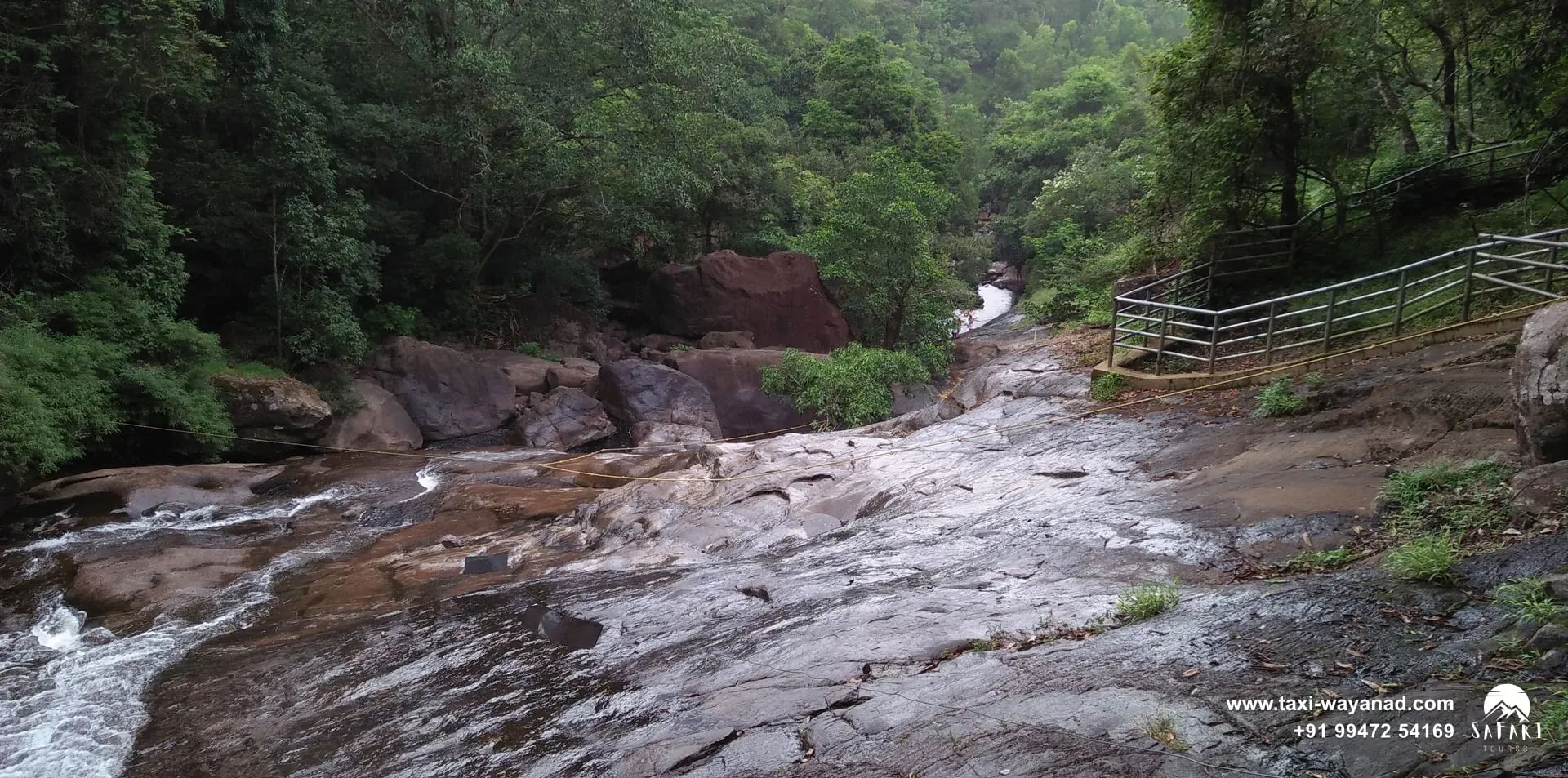 Stream flowing over rock slabs with a railed walkway above Meenmutty Waterfalls, Wayanad